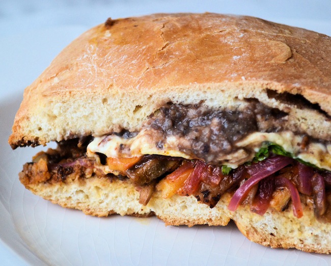 A closeup of a vegan Pibil Torta Sandwich showing black bean sauce and melted vegan cheese.