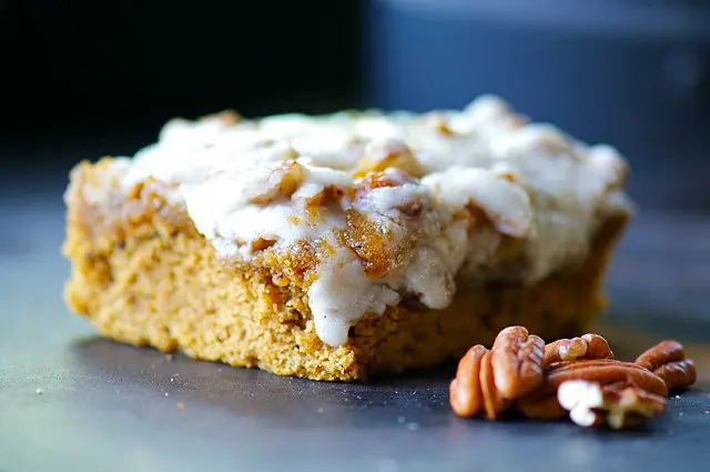 a pumpkin blondie with frosting on a dark countertop.