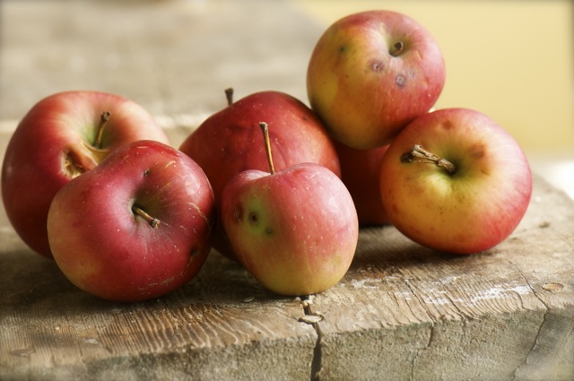 Several apples sit on a wooden table.