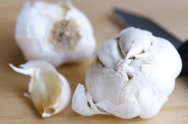 Two garlic bulbs on a cutting board next to a knife.