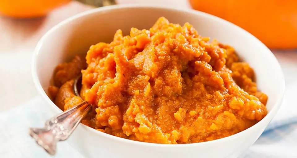 A bowl holds pumpkin puree and a spoon. There's a pumpkin in the background.