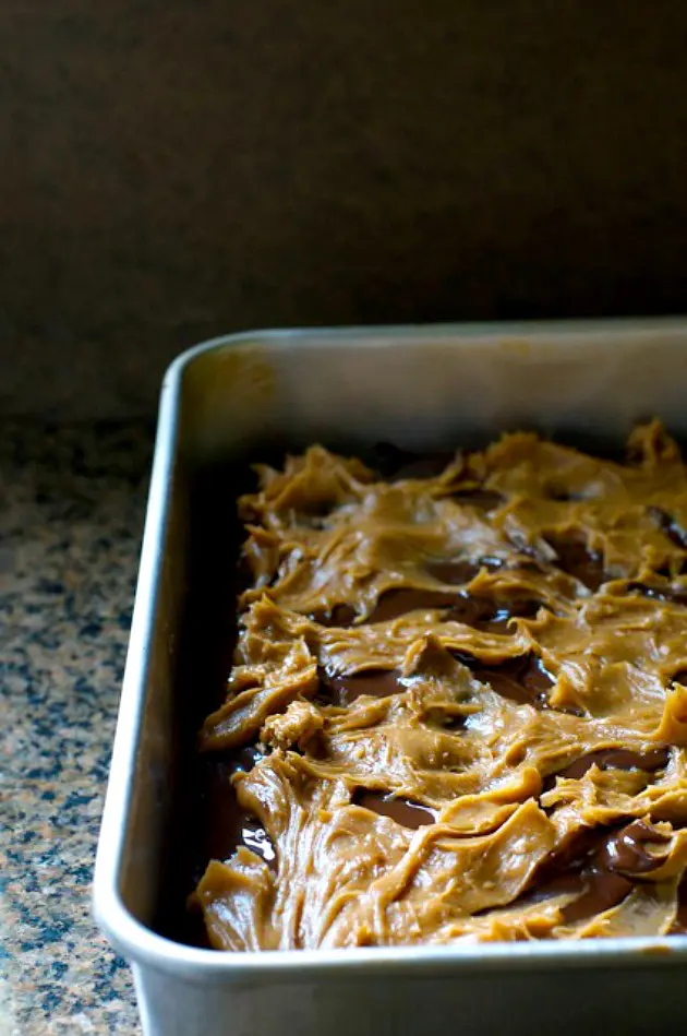 A peanut butter sauce has been spread over brownies in a pan.
