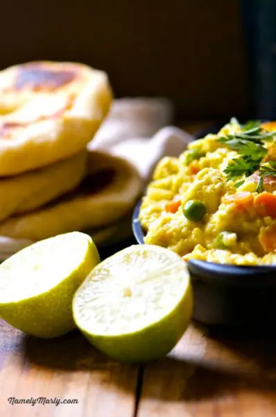 A serving dish full of chickpea curry sits next to naan bread and limes.