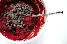 Chocolate chips are in a bowl with red velvet batter.