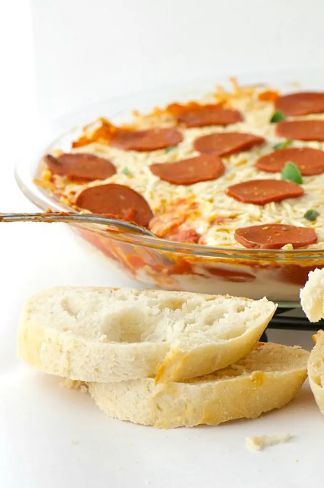 Slices of bread sits in front of a pie dish full of vegan pepperoni pizza dip.