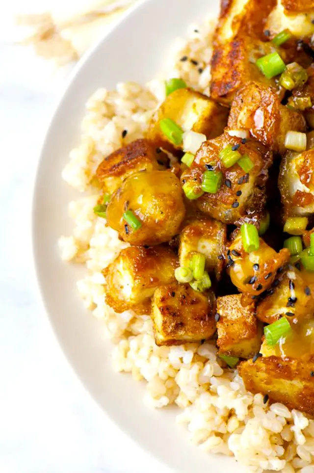Crispy Orange Tofu on a bed of rice with sliced green onions on top.