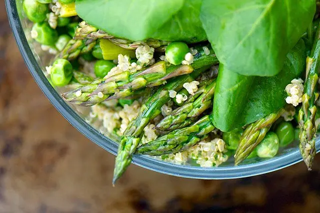 Looking down on a bowl of quinoa with asparagus and peas and fresh spinach leaves.