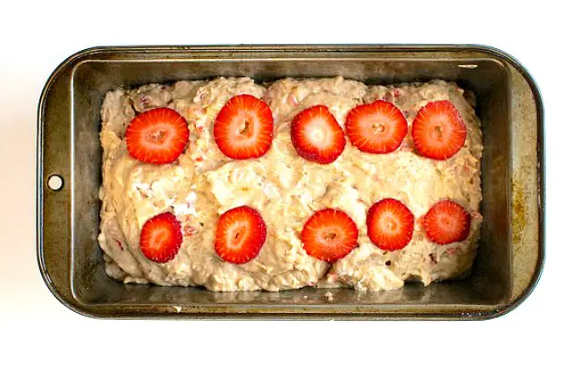 Looking down on a loaf pan full of batter, with sliced strawberries on top.