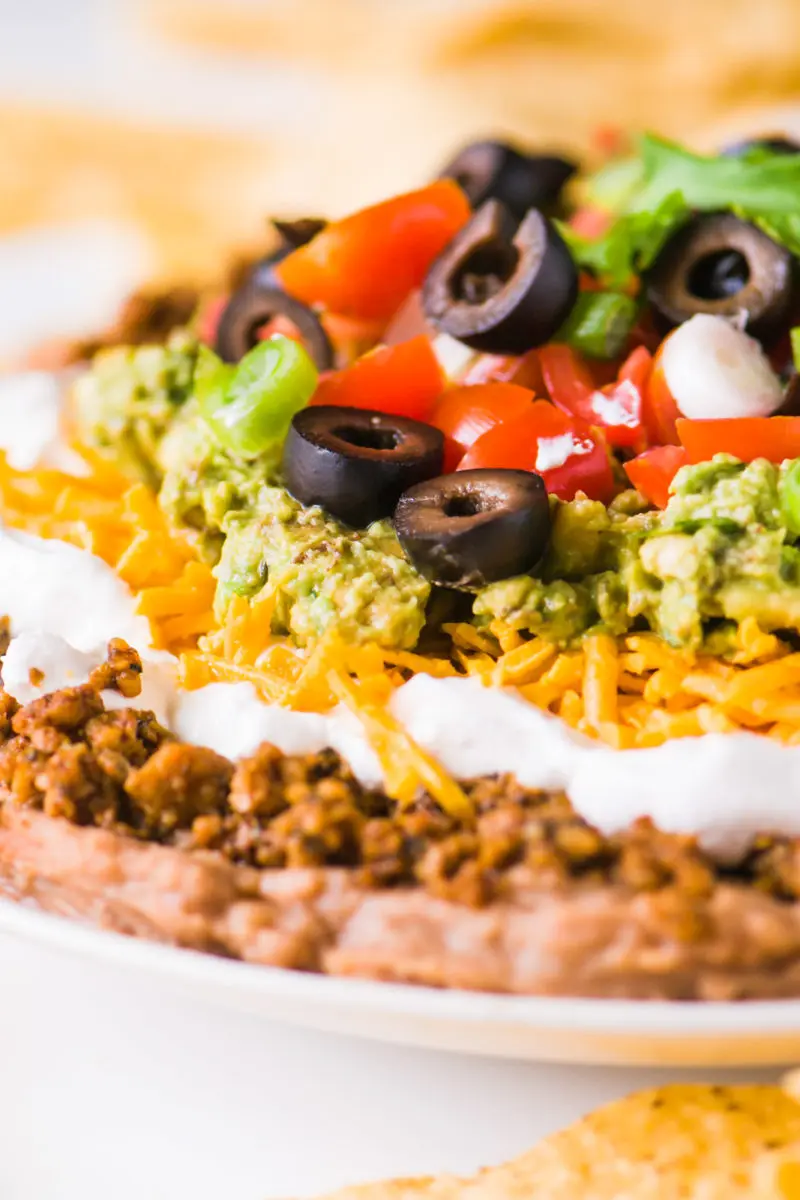 A close-up shot of vegan 7 layer dip shows layers of beans, veggie crumbles, and more toppings.