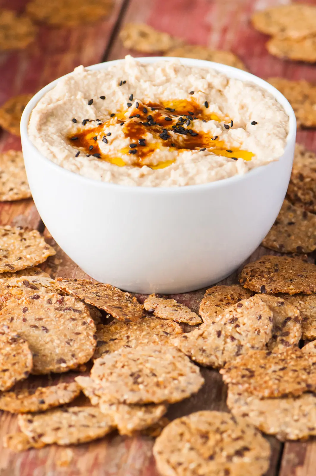 A bowl of smoky chipotle hummus is surrounded by multi-grain crackers.