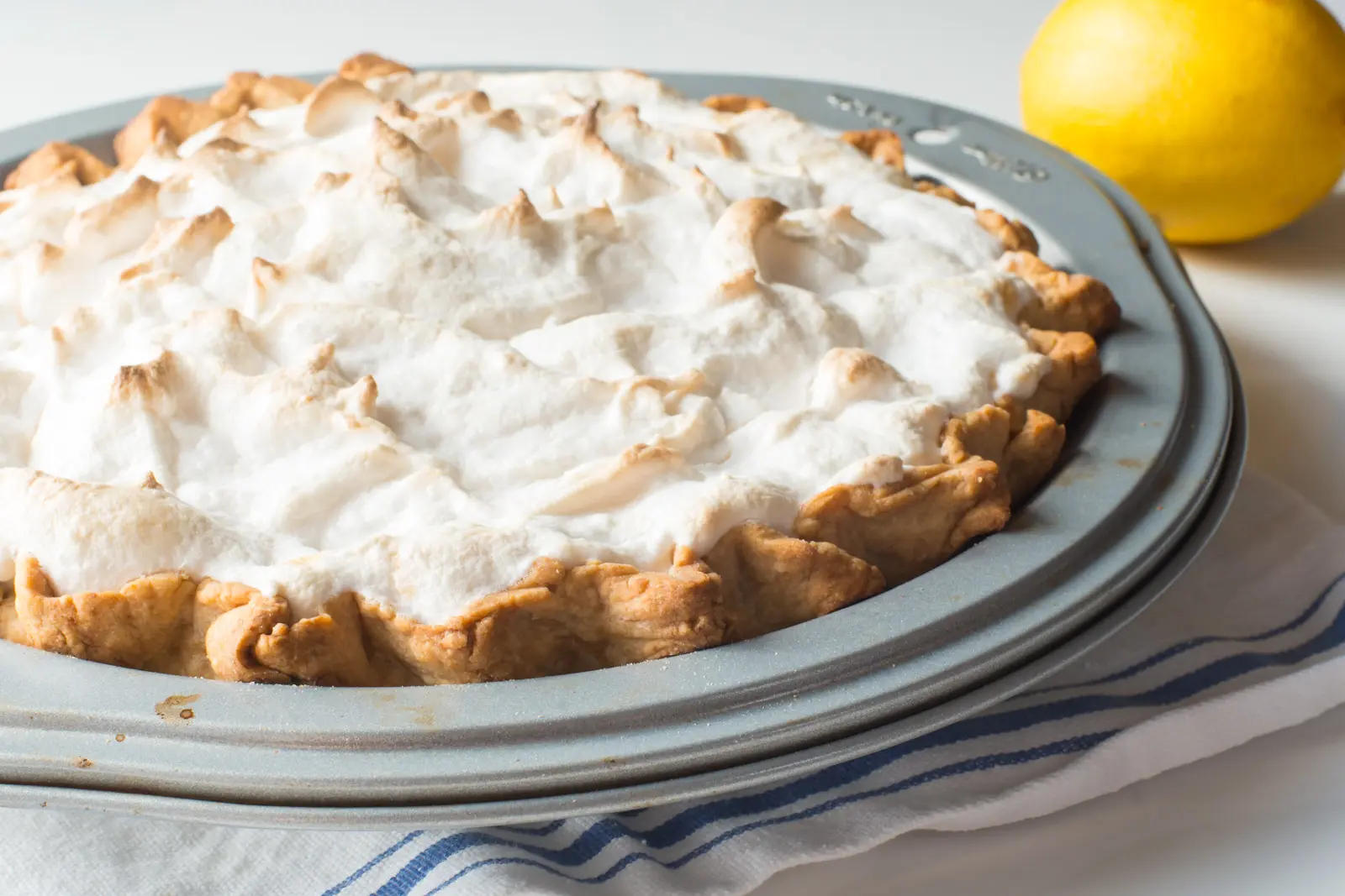 A pie topped with vegan meringue is in a pie dish. A lemon is behind it. 