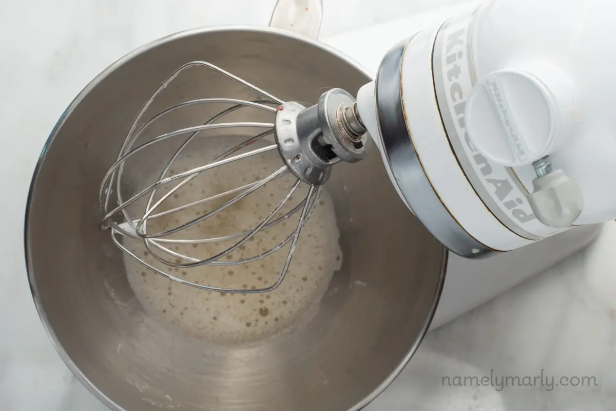 Looking down on a stand mixer with a foamy chickpea liquid mixture in the bottom.