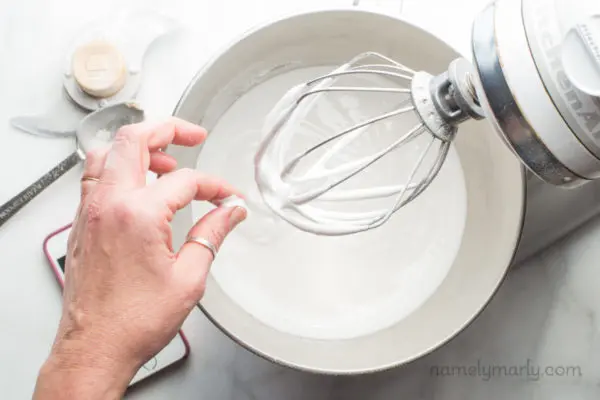 A hand pinching homemade vegan whipped meringue in a mixer