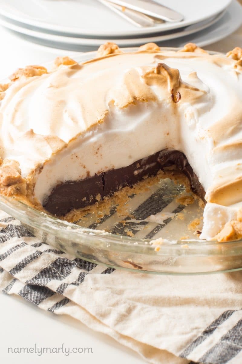 A pie has a slice cut out, showing chocolate pudding a meringue on top.