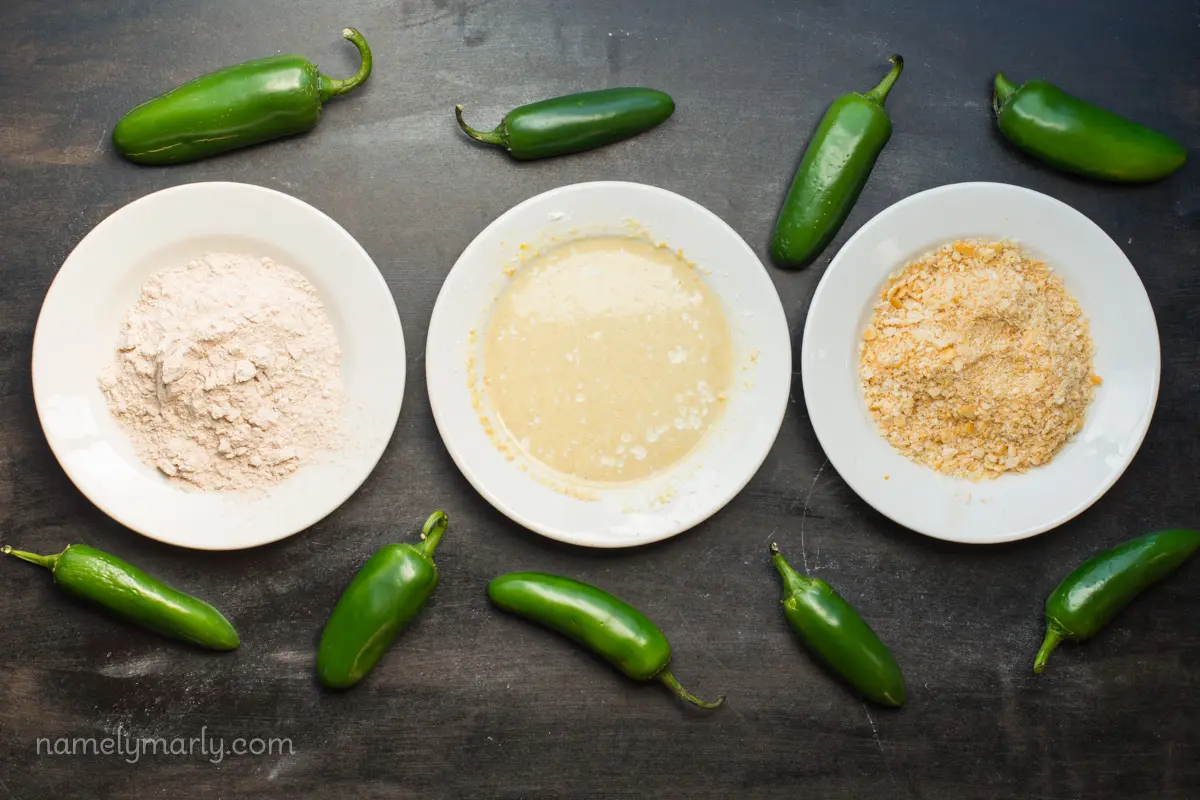 Three plates hold different dipping ingredients. There are several green jalapeños around the plates.