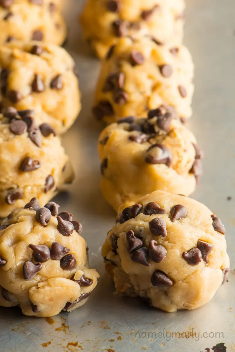 Several cookie dough balls in rows on a baking sheet.