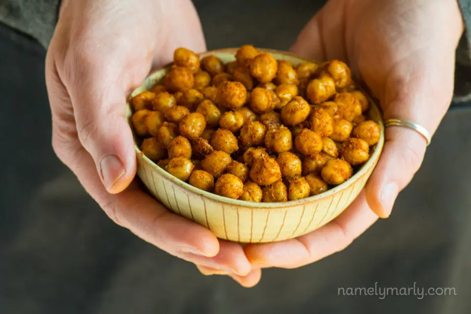 Two hands hold a bowl full of roasted chickpeas.