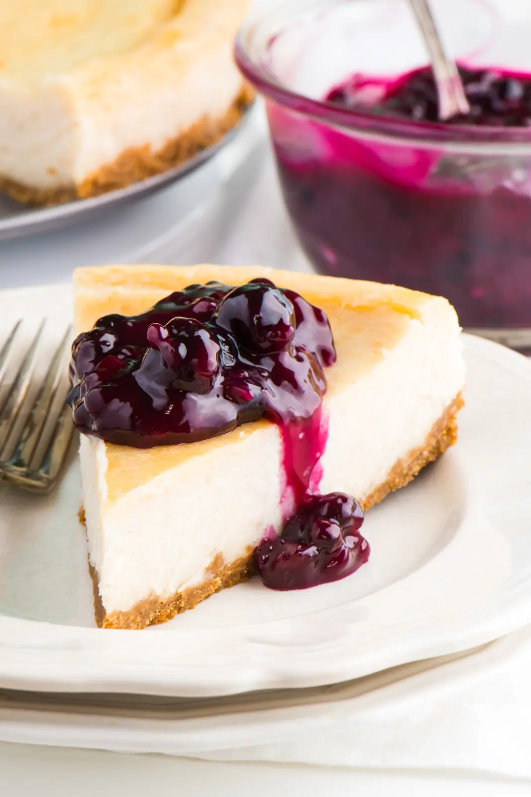A slice of vegan New York style cheesecake sits on a plate with blueberry sauce over the top.