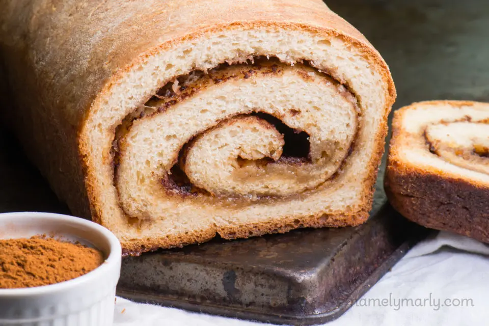 A loaf of cinnamon bread with a slice cut off showing swirls of cinnamon inside.