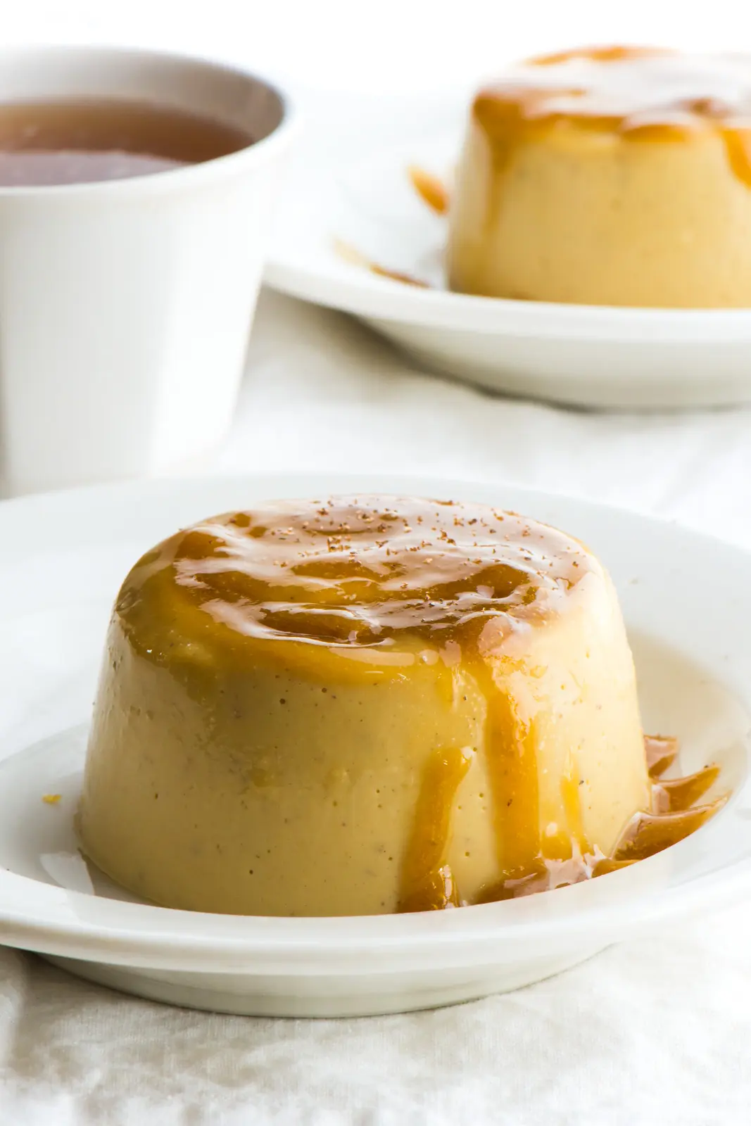 A closeup of vegan flan with caramel topping. Another plate is behind it.