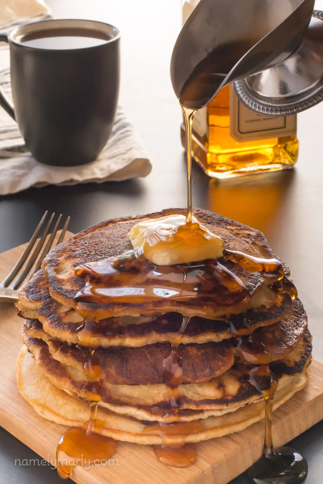 Pouring syrup over vegan pancakes with a mug of tea behind it.