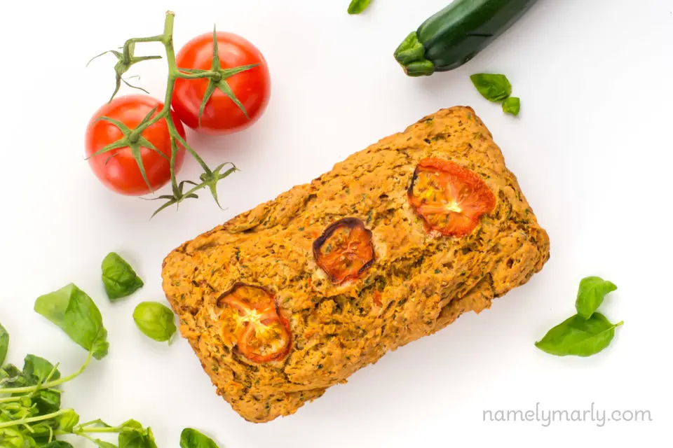 Looking down on a loaf of savory zucchini bread next to fresh spinach, zucchini and tomatoes.