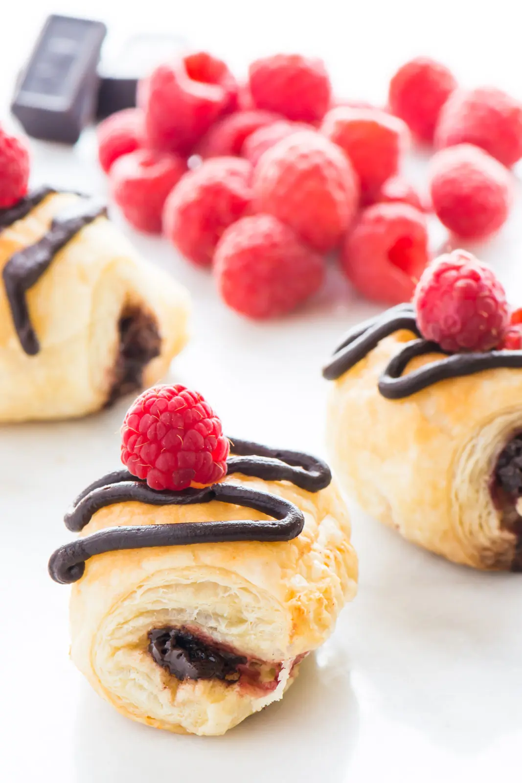 Several croissants show chocolate in the middle and red raspberries on top with a drizzle of chocolate glaze.
