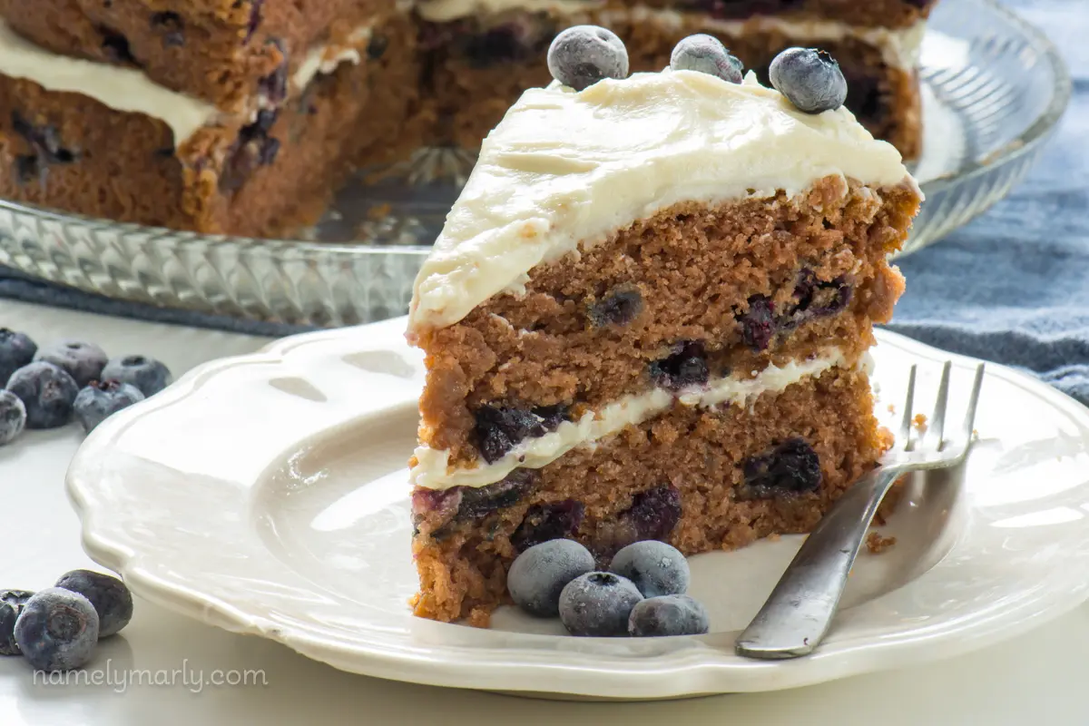 A slice of 2-layer cake on a white plate with fresh blueberries around it.