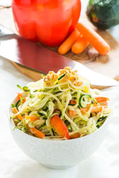 Zucchini Noodles Pad Thai is in a bowl in front of a red bell pepper and other ingredients.