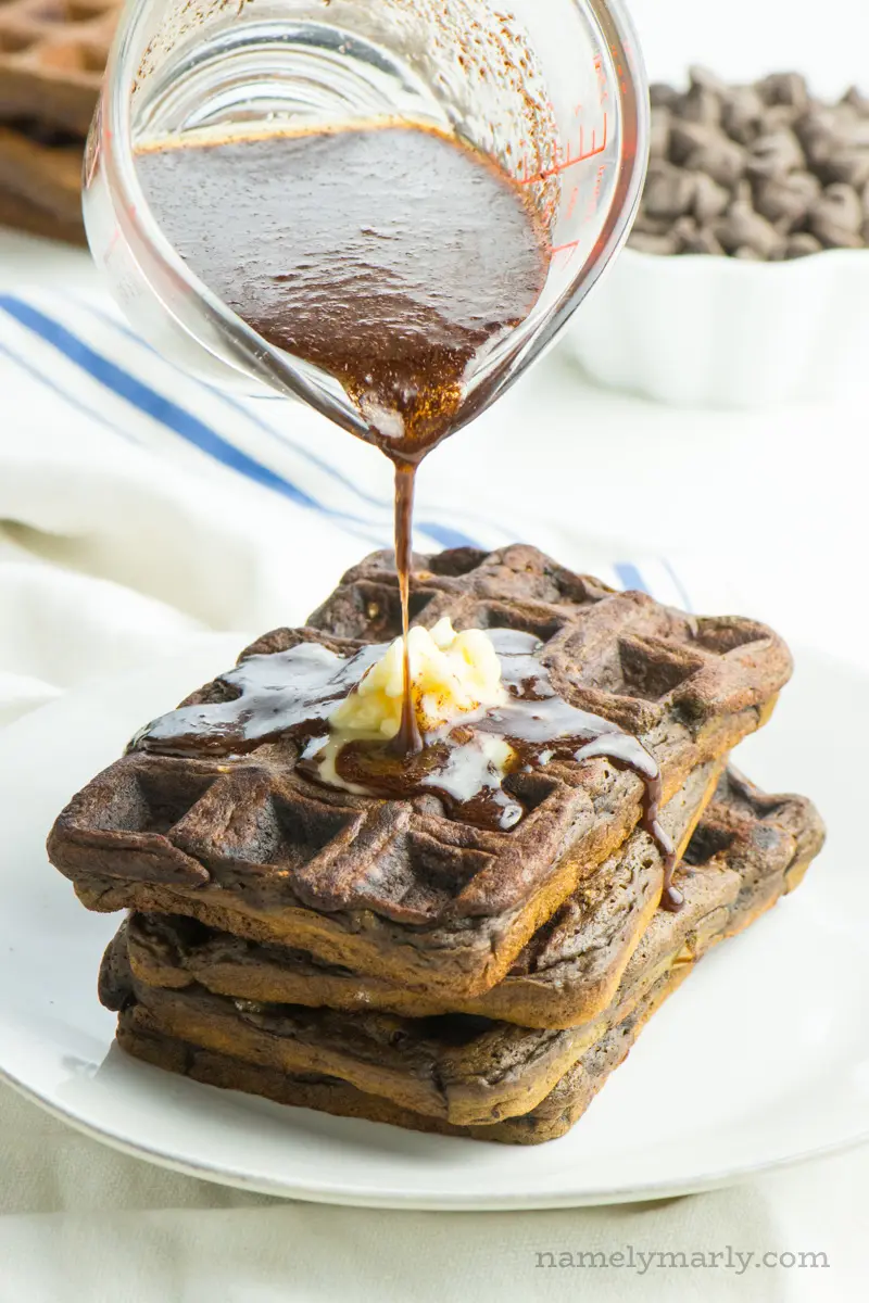 Pouring chocolate maple syrup over a stack of chocolate waffles.