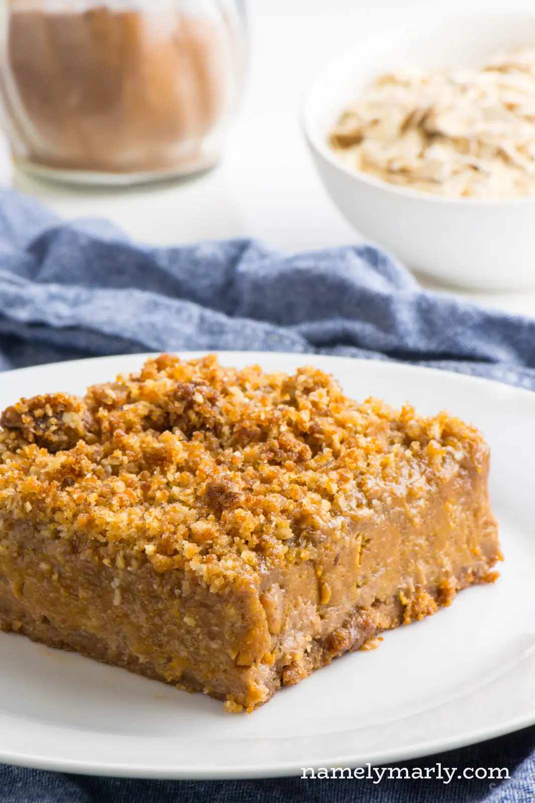 One slice of these vegan pumpkin pie bars sits on a plate with oatmeal and spices behind it.