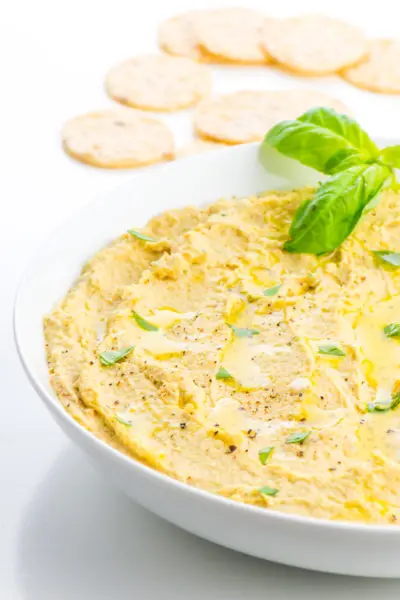 A large bowl holds hummus with a few basil leaves on top and crackers around it.