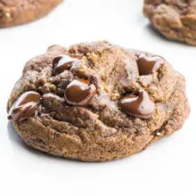 A close-up look at a vegan chocolate chocolate chip cookie with several more in the background.