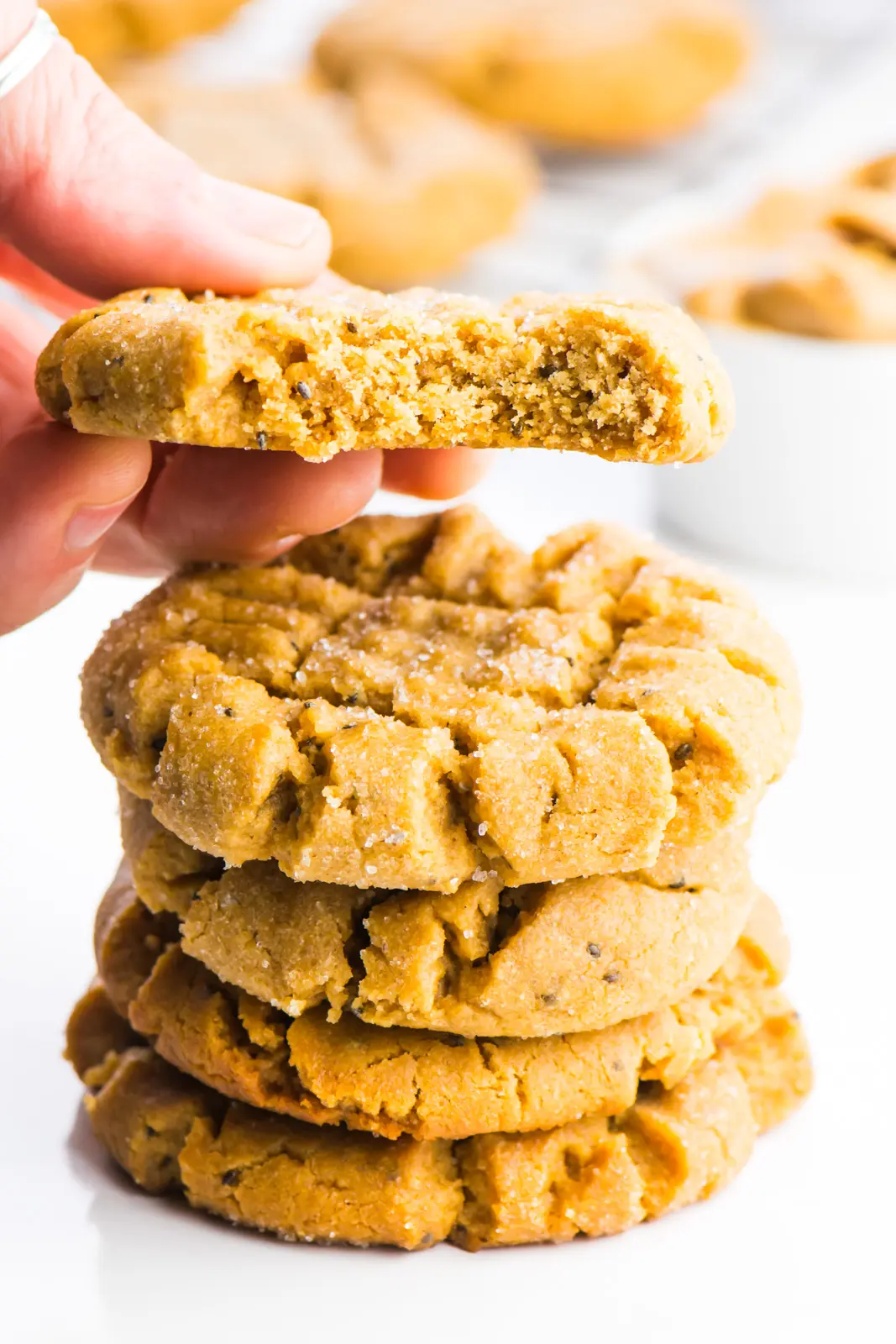 A stack of vegan cookies is sitting in the foreground. A hand is holding a cookie right above the stack and there's a bite taken out of that cookie.
