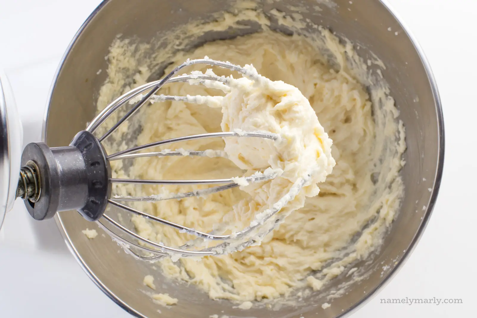 A stand mixer has been used to make cookie dough. The cookie dough is in the stand mixer bowl, and the mixer attachment is full of cookie dough too.