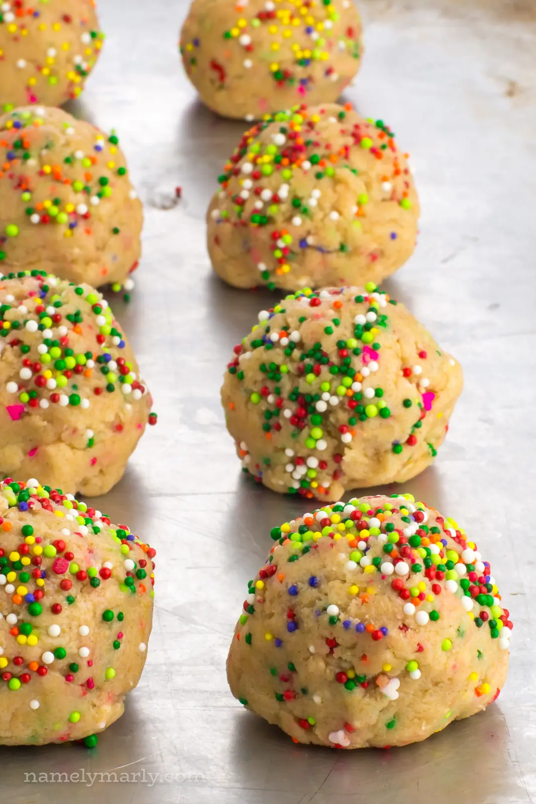 Several confetti cookie dough balls are lined up in rows on a cookie sheet, waiting to be placed in the oven.