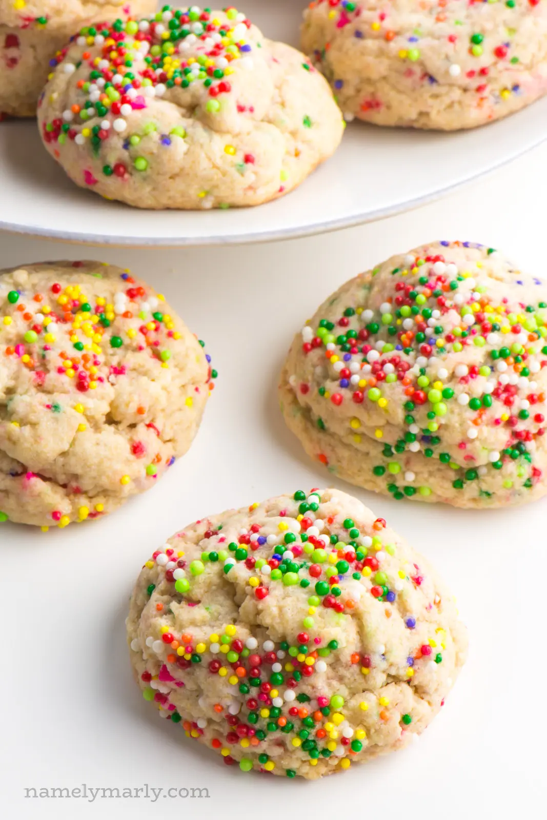 Three funfetti cookies on a counter with a plate behind them full of more cookies.