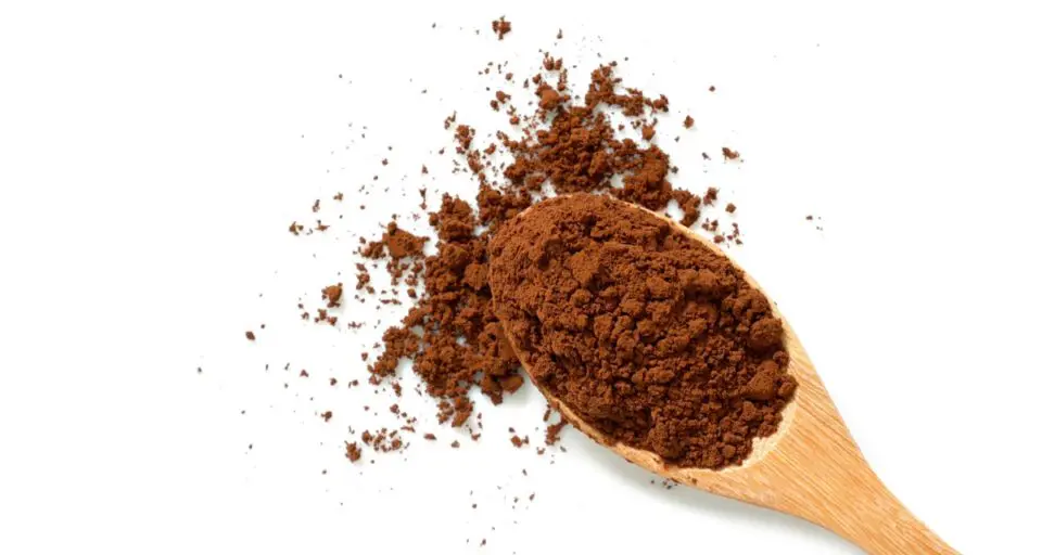 Looking down on a wooden spoon full of cocoa powder, spilling the powder out onto the table around it.