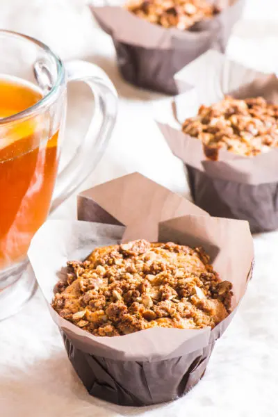 A coffee cake muffin sits next to a cup of hot tea, with other muffins around it.