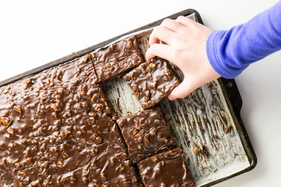 A hand reaches in to grab a slice of this vegan Texas sheet cake straight from the pan!
