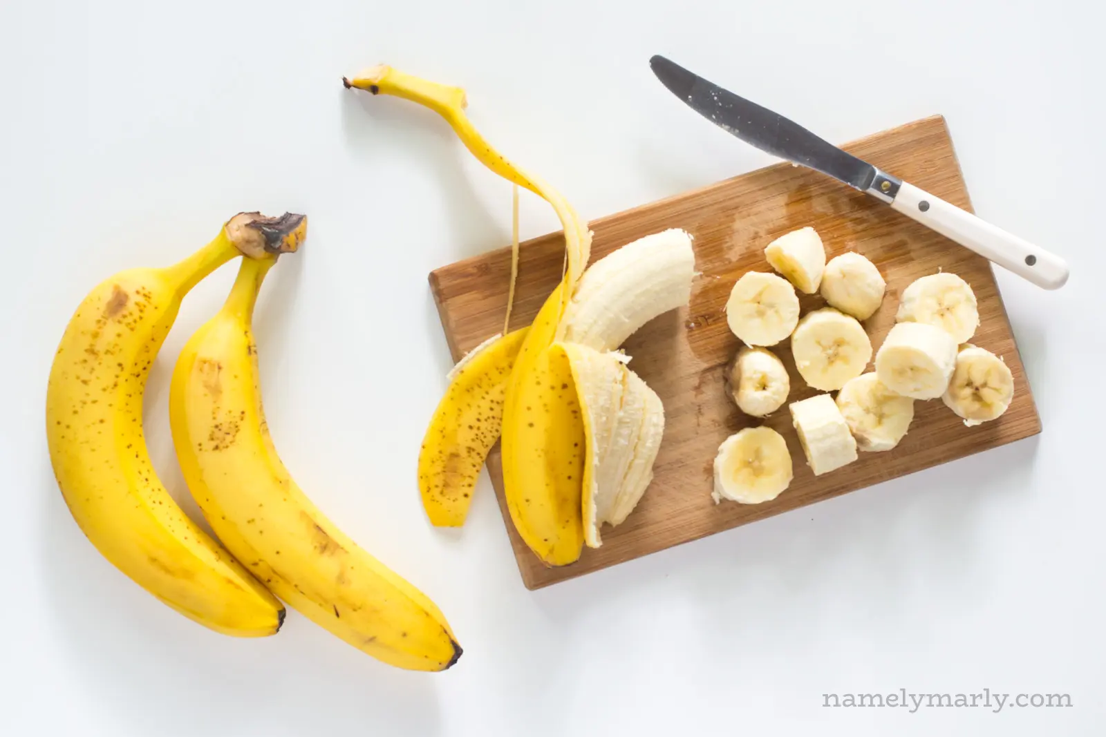 A banana on a cutting board with several chopped bananas next to it.