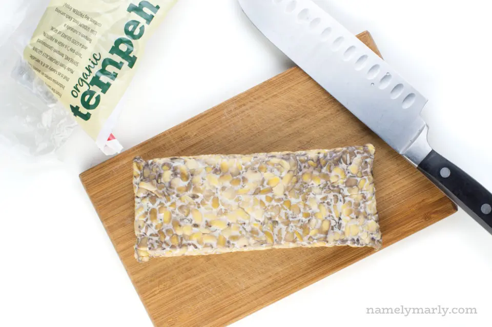A block of tempeh on a cutting board next to a knife.