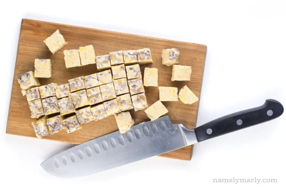 Tempeh chopped into cubes sitting next to a knife on a cutting board.