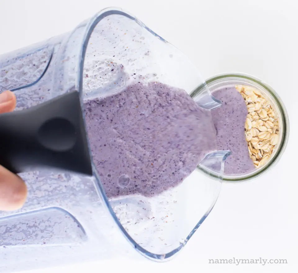 The blueberry milk from the blender is being poured over a bowl of oatmeal.