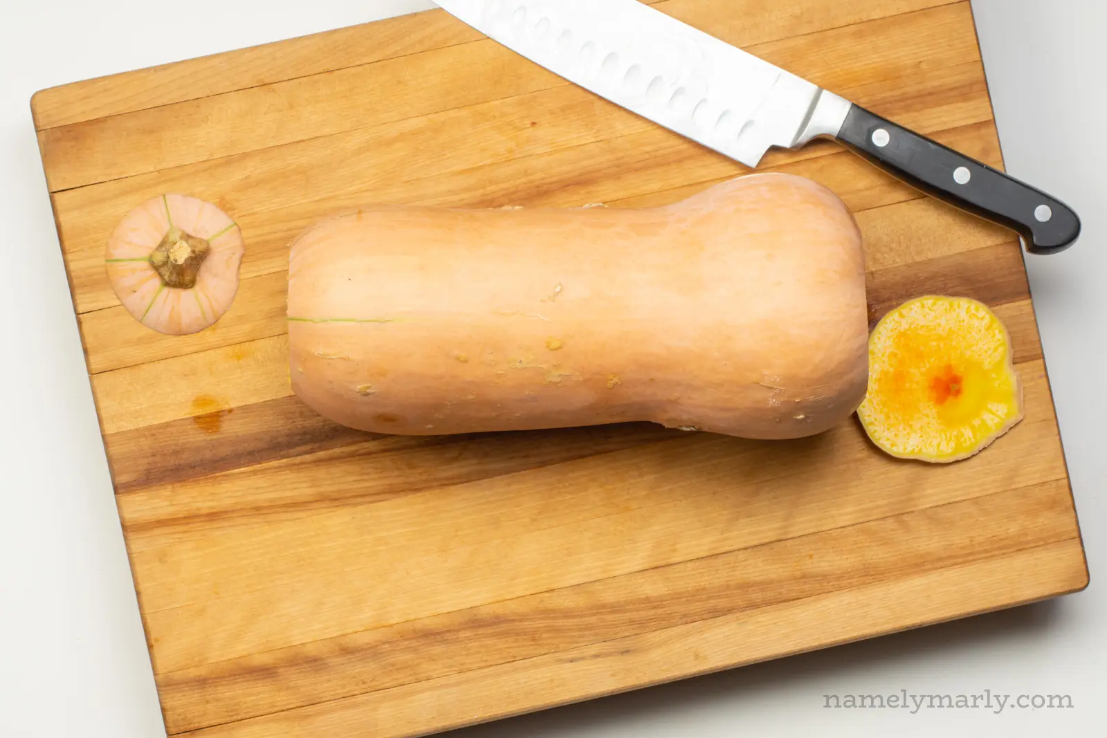 A butternut squash on a cutting board with the top and a sliver off the bottom removed.