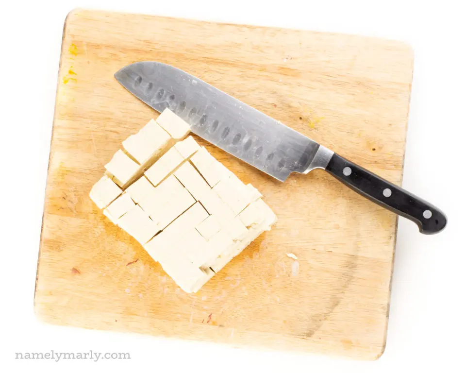 A block of tofu on a cutting board after being sliced into cubes.