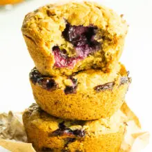 Three vegan blueberry muffins are stacked on top of each other and a bite is taken out of the top one.