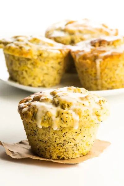 A vegan orange poppyseed muffin on a piece of brown pepper with more muffins behind it.