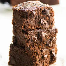 A stack of vegan brownies with several more brownies behind them.