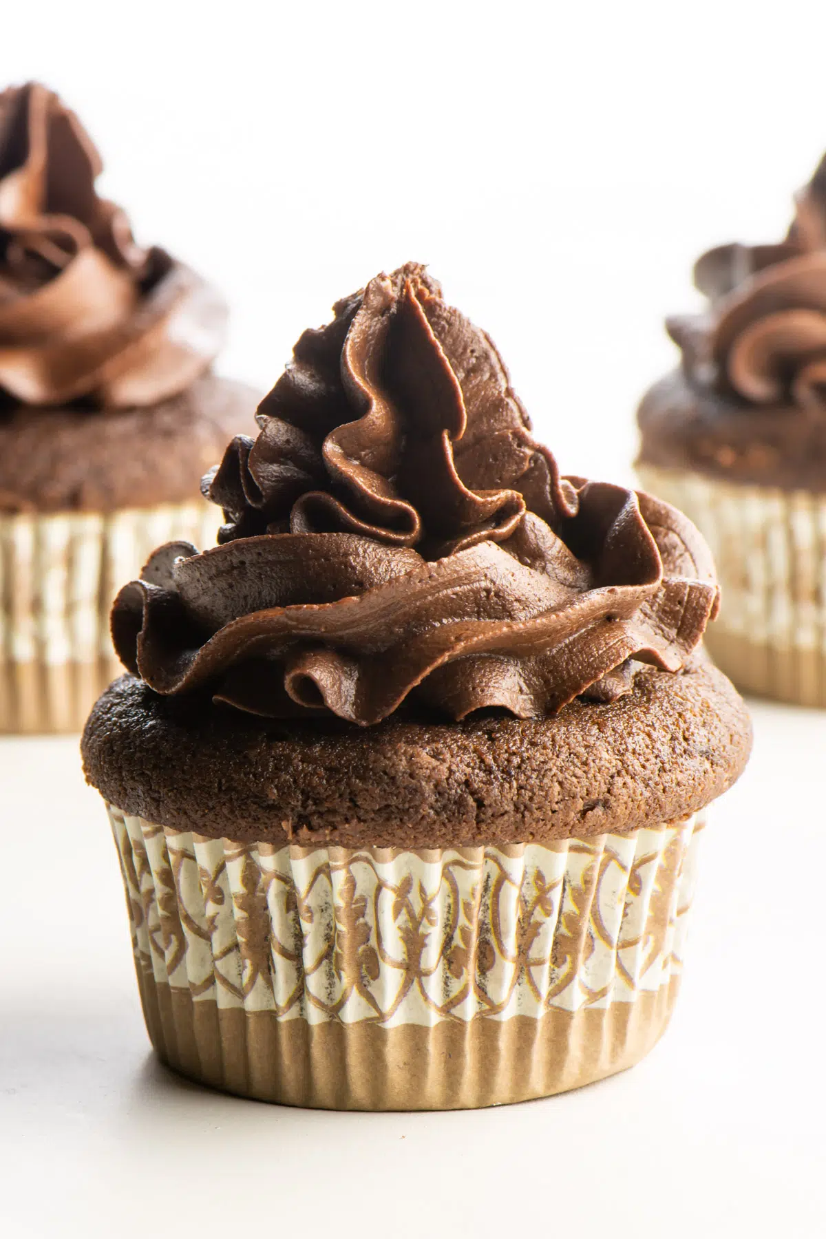 A cupcake with chocolate frosting sits in front of two other cupcakes.
